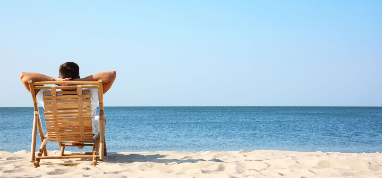 Young man relaxing in deck chair on sandy beach