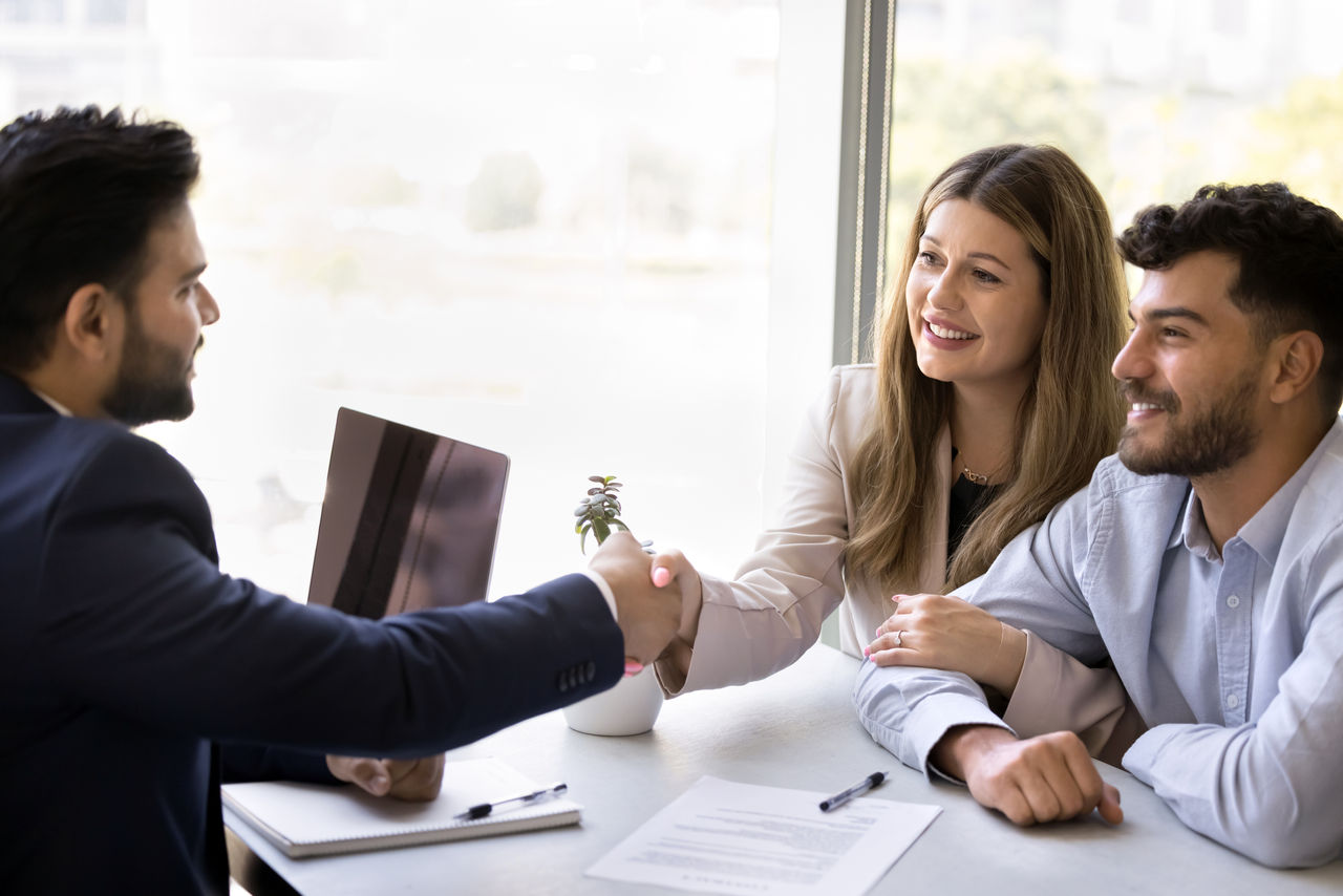 Cheerful satisfied diverse couple of clients shaking hands with Indian lawyer man, legal expert, meeting with specialist for consultation, getting agreement, giving handshake, thanking, smiling